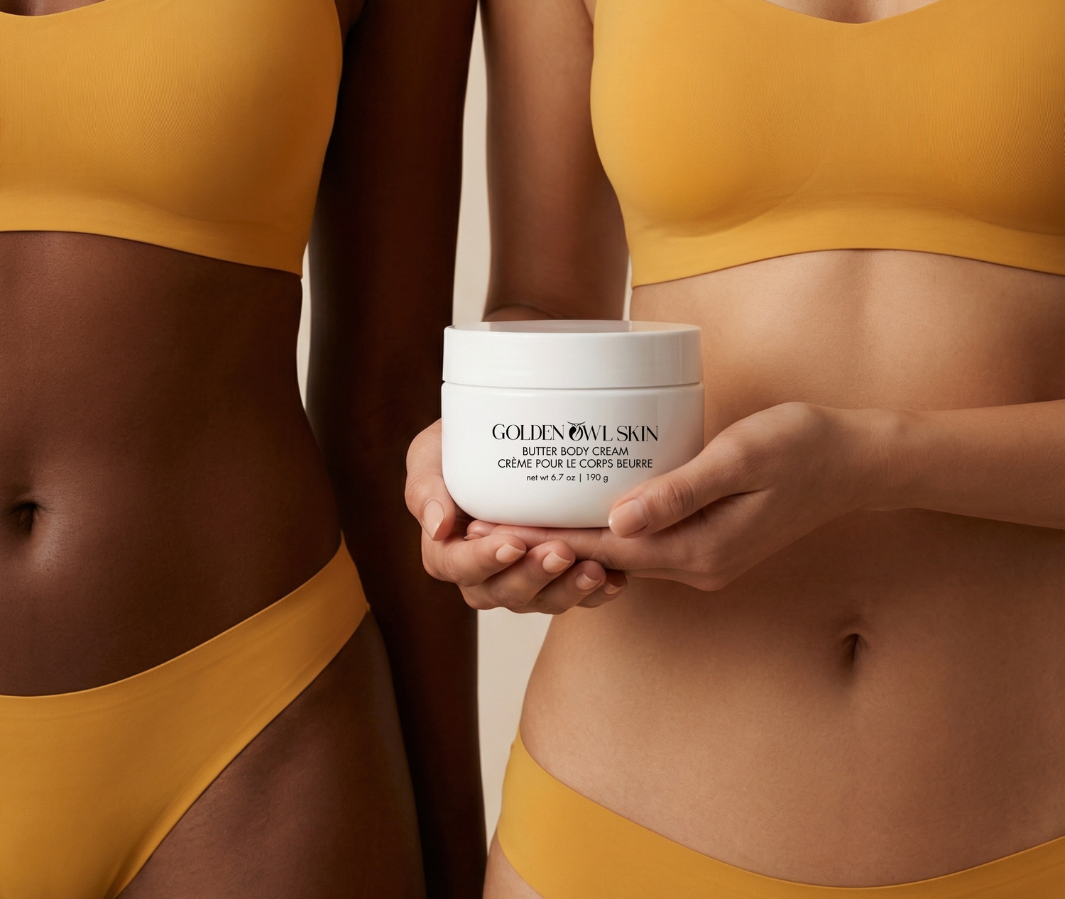 Two people wearing yellow swimsuits holding a jar of Golden Owl Skin Butter Body Cream.